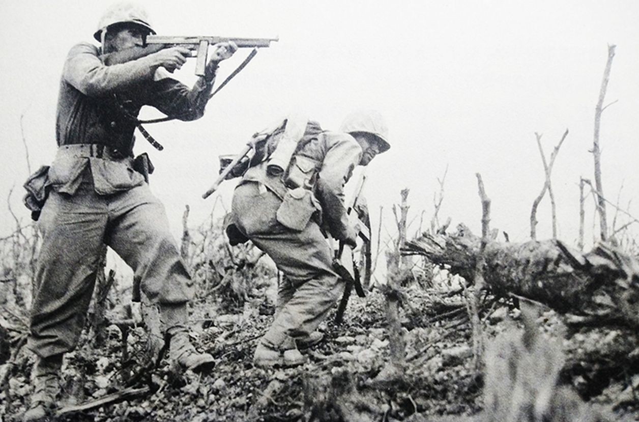 1945年,太平洋战场,装备M1A1汤普森冲锋枪的美国海军陆战队士兵在战场上冲锋陷阵,其中一名士兵正举枪射击。
