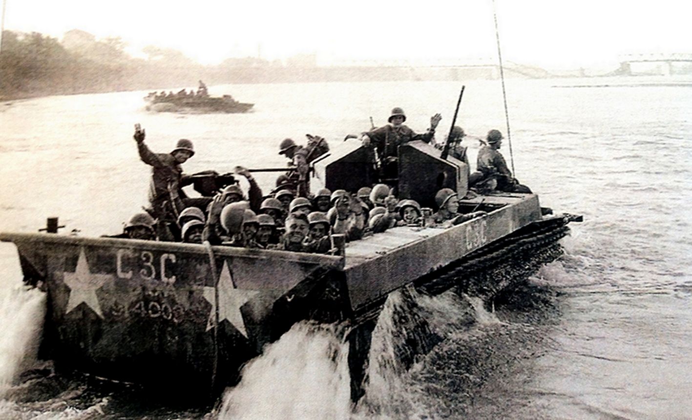 1945年4月26日，欧洲西线战场，正在水中行驶的一辆LVT4两栖装甲车。吸取太平洋战争经验，为使机枪手在操作机枪时得到保护，该辆LVT4的两挺机枪都装上了全防护钢板；车上美军士兵向镜头竖起胜利的「V」形手势，显示盟军已到胜利时刻。