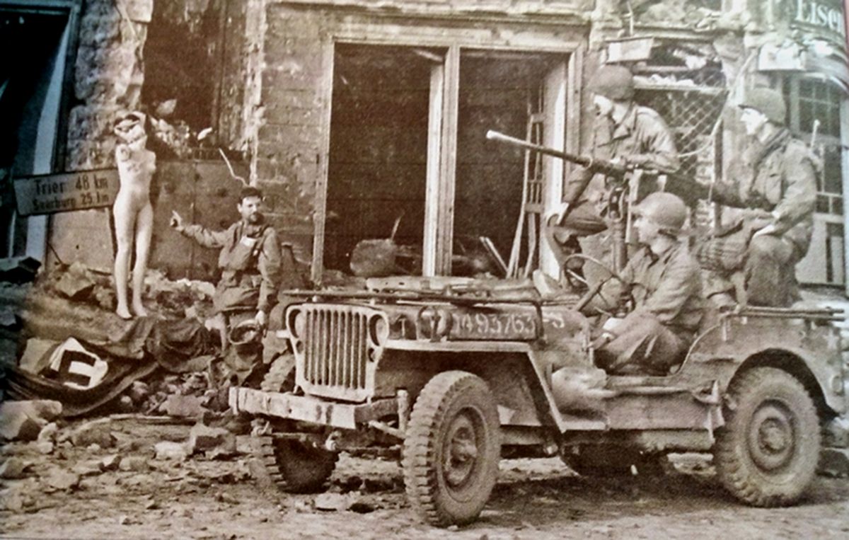 1945年3月,「莱茵河战役」期间,美军第26师第328步兵团的威利吉普车士兵进入刚结束战斗的德国特里尔(Trier)城镇,正在观看路边一服装店的假人。