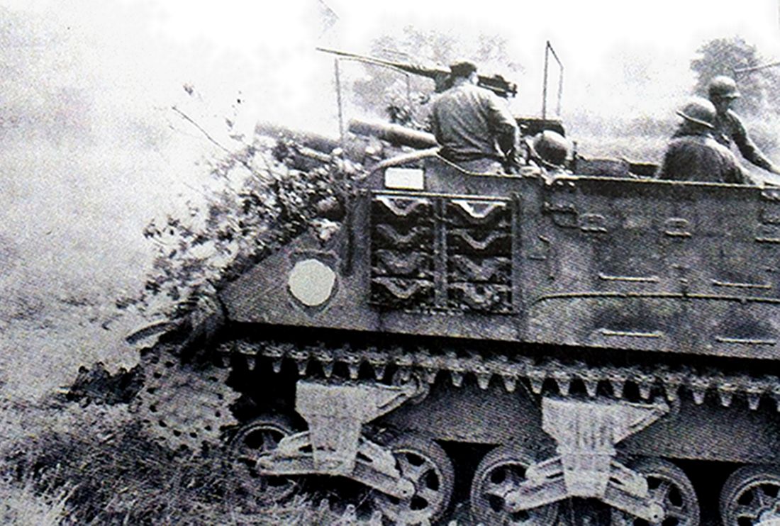 1944年8月，「布列塔尼战役」期间，正在圣波瓦附近作战的美军一辆M7自行火炮，炮车上的炮组成员正在敞开式炮塔操作105毫米榴弹炮向敌方阵地开炮。