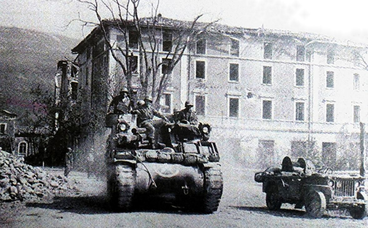 1945年4月，「莱茵兰战役」期间，美军第一装甲师的一辆M7自行火炮正行驶在德国城镇「韦尔加特」的街道上。