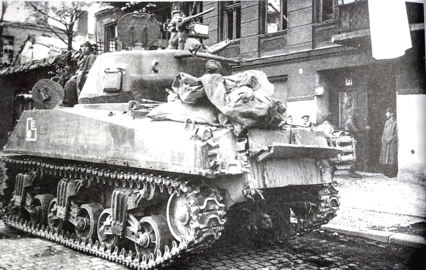 1945年,「柏林战役」期间,一辆苏军的M4中型坦克正在进入德国首都柏林市区街道。注意:此刻路边居民楼上已经挂上了一面白旗,证明此街区已被苏军攻占。