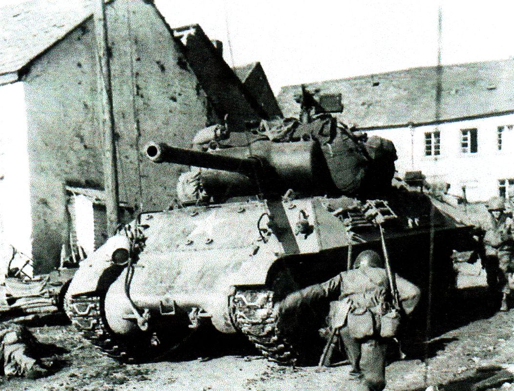 1945年3月15日,德国Schillingen地区,第三集团军94师301步兵团的一群士兵依靠一辆M36坦克歼击车的掩护,躲避德军的炮弹碎片,这辆炮车正在这个城镇里等待前往德国Kell镇的命令。