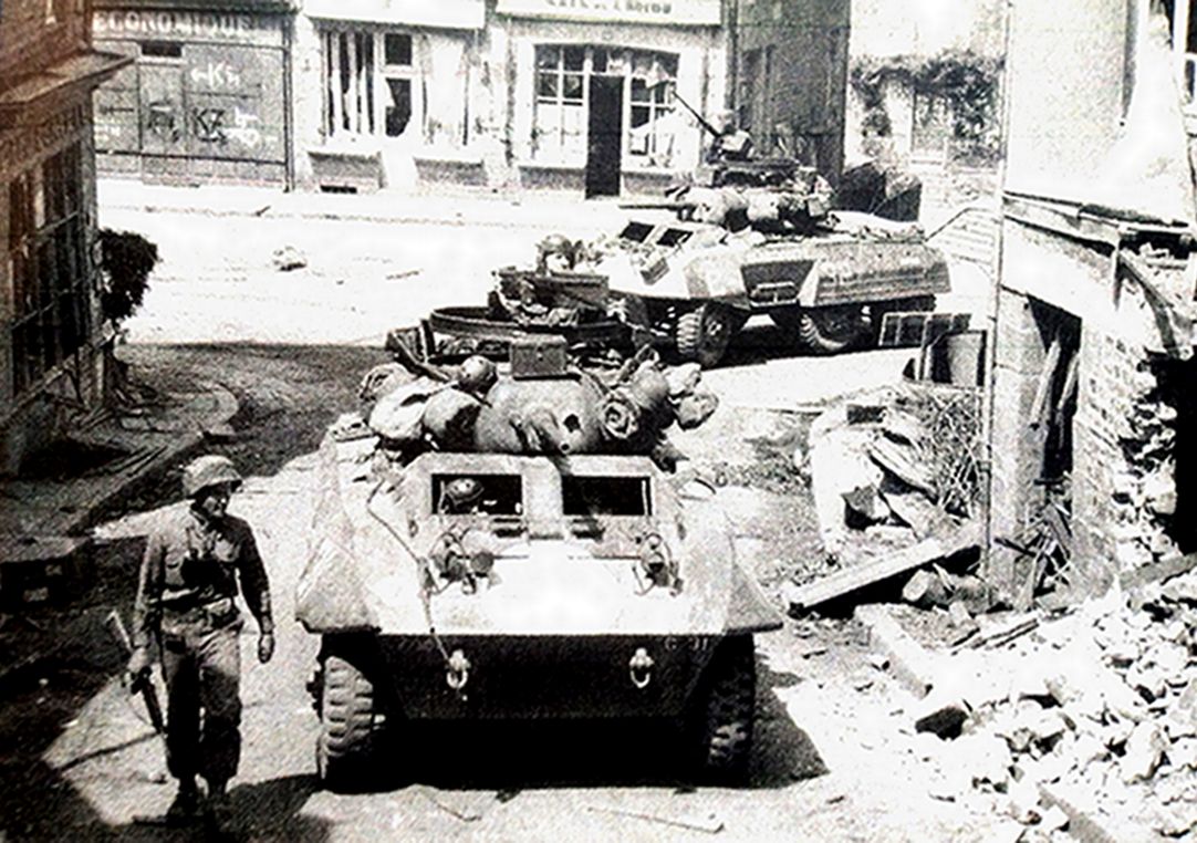 1944年8月3日，「诺曼底战役」期间，眼镜蛇行动中，美国第2装甲师第82骑兵侦察营的2辆M8轮式装甲车正穿过法国诺曼底地区的圣瑟韦－卡尔瓦多斯社区（St.Sever Calvados）的一个路口。注意：装甲车炮塔上加装了一个挂载机枪的钢环。