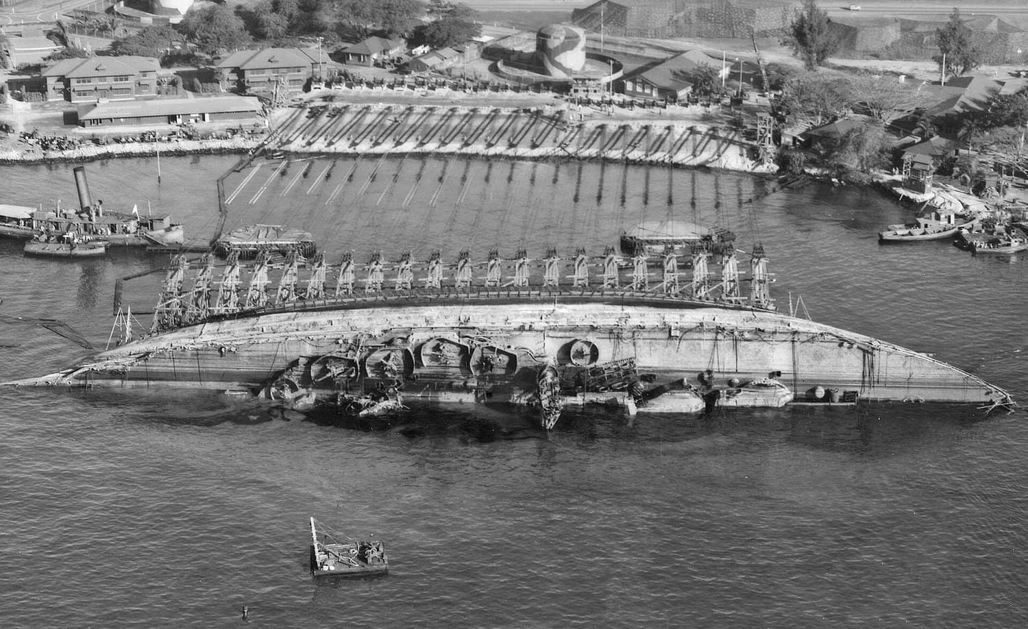 1943年3月19日,珍珠港海军造船厂开展「俄克拉何马」号战列舰(BB-37)打捞作业的航拍视角,该视角朝福特岛(Ford Island)方向,可见舰船已扶正至一半的状态。