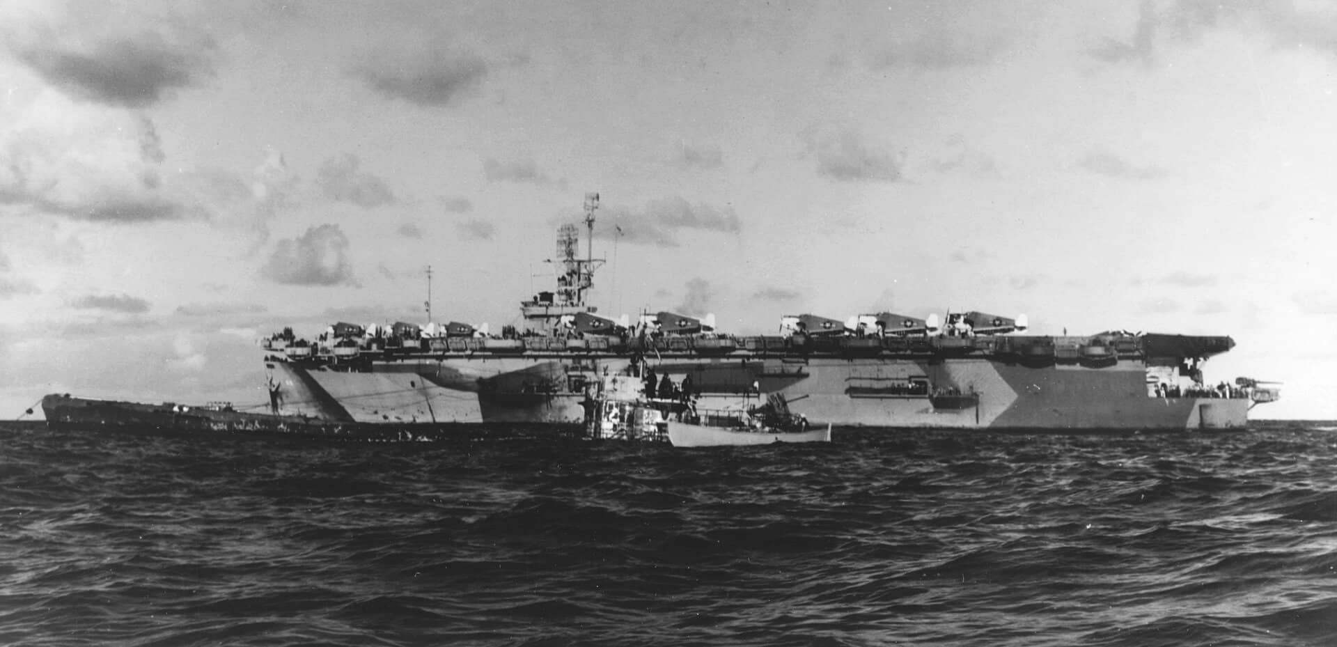 1944年6月4日,大西洋,「瓜达尔卡纳尔」号护航航空母舰(CVE-60)的舰员在舷侧查看被俘的德国 U-505 号潜艇。当日该舰猎潜群迫使 U-505 浮出水面并登艇俘获,缴获德军密码本与「恩尼格玛」密码机。注:「瓜达尔卡纳尔」号此时采用的是「第32号伪装方案4A式样」(Camouflage Measure 32, Design 4A)迷彩方案。