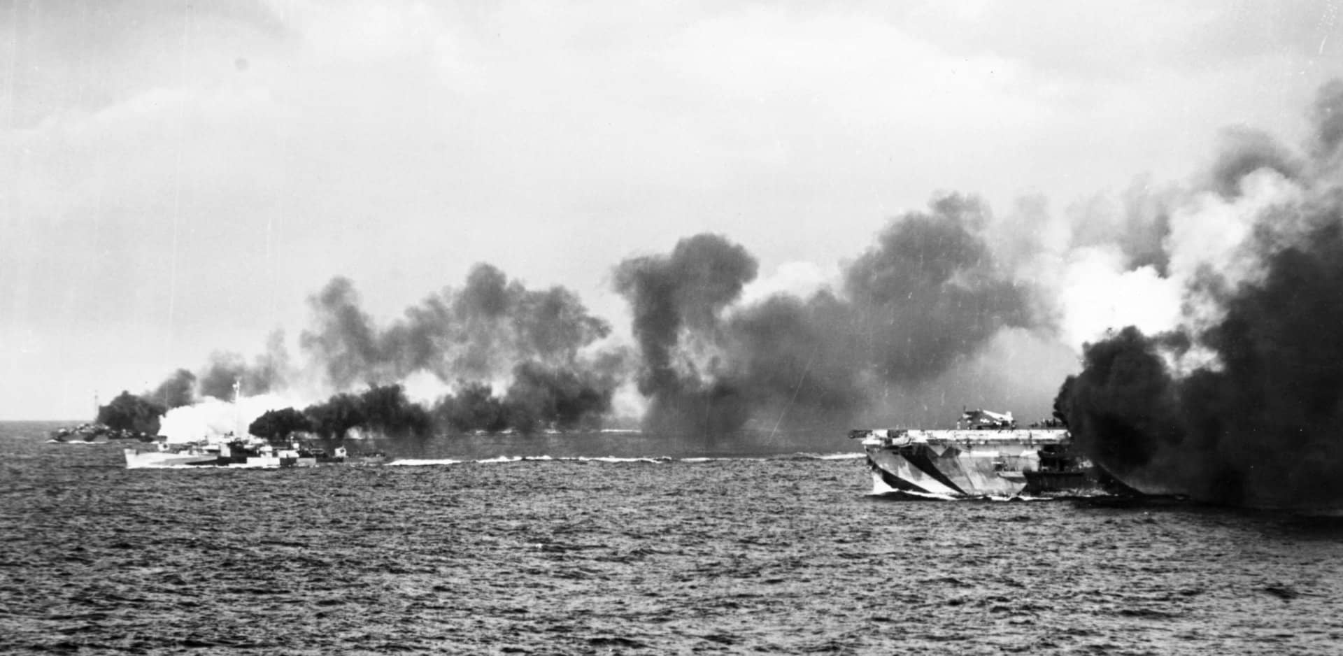 1944年10月25日,萨马岛海战期间,图片右侧的美国海军「甘比尔湾」号护航航空母舰(CVE-73)及其护航舰艇施放烟幕掩护登陆编队撤退。此时「甘比尔湾」号采用的是「第32号伪装方案15A式样」(Camouflage Measure 32, Design 15A)迷彩方案,左侧较近的那艘护航驱逐舰是采用「第2C号伪装方案」(Camouflage Design 2C)的「雷蒙德」号(USS Raymond,DE-341)。另一艘护航驱逐舰则采用「第22D号伪装方案」(Camouflage Design 22D)迷彩方案,应是「丹尼斯」号(USS Dennis,DE-405)或「塞缪尔·B·罗伯茨」号(USS Samuel B. Roberts,DE-413)的其中一艘。