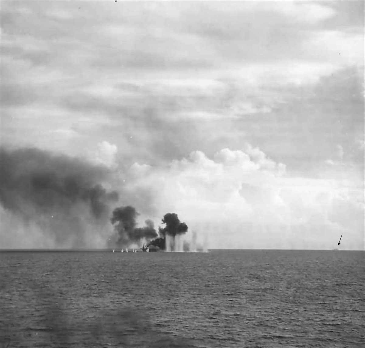 1944年10月25日,「甘比尔湾」号护航航母(CVE-73)在萨马岛外海被日军舰炮命中后起火。该舰主机被毁、航速下降,最终被追击的日舰击沉。注:图中是日本战列舰「大和号」发射的一发18.1英寸(46厘米)炮弹齐射落在该舰左舷附近,而六枚较小口径炮弹的齐射则落在该舰前方。此外,远处指头所指处依稀还可以看到一艘加入围攻的日本巡洋舰。