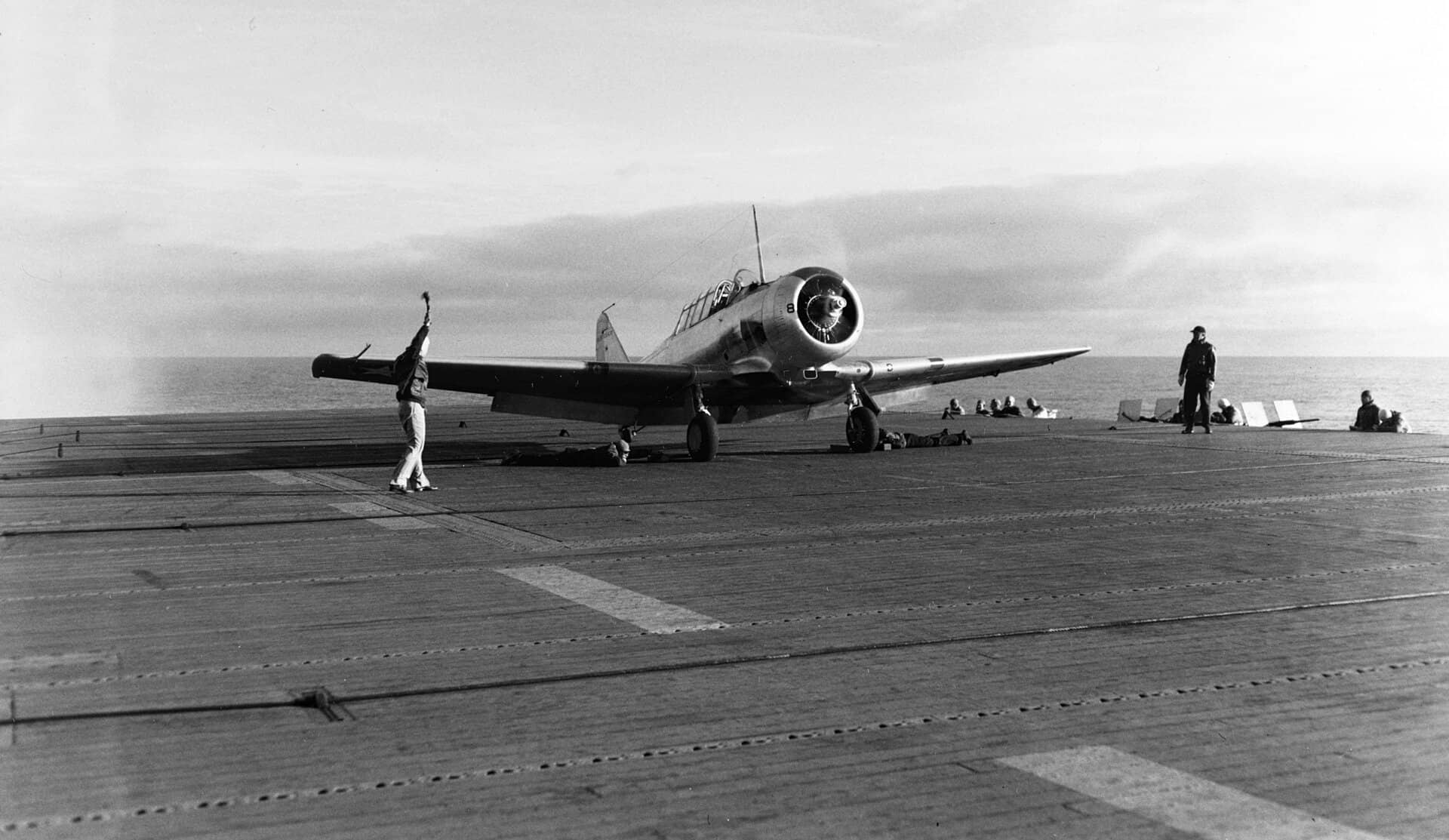 1943年1月28日,加利福尼亚州圣迭戈外海,一架 SNJ-3 教练机正从「长岛」号(ACV-1)起飞,执行飞行员舰上起降资格训练。注:自从1943年9月20日「长岛」号返回美国西海岸后,即在圣迭戈开始负责培训舰载机飞行员的任务。1944年至1945年间,它还负责承担将飞机及机组人员从西海岸运送至太平洋各处前哨基地的运输任务。日本投降后,美国海军执行「魔毯行动」(Operation Magic Carpet),「长岛」号又重返各个海外基地,负责将美军官兵运送回国。